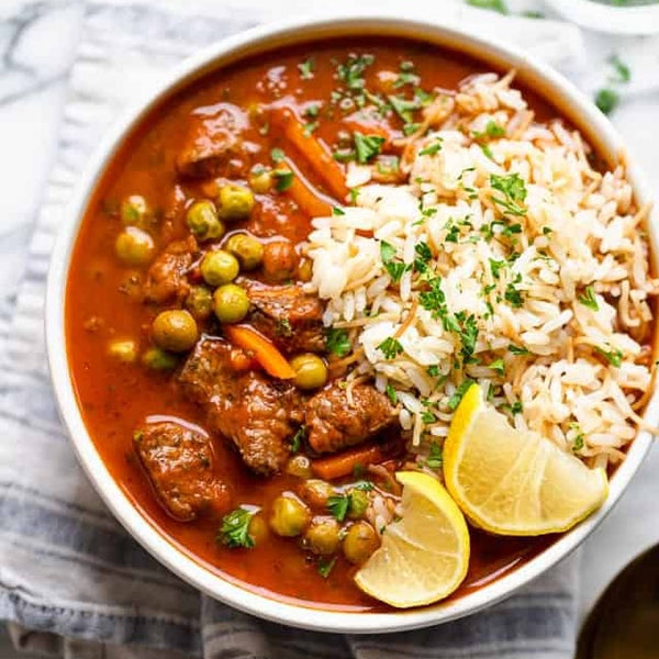 A bowl of Lebanese peas and carrots stew in tomato sauce served with rice and lemon wedges.