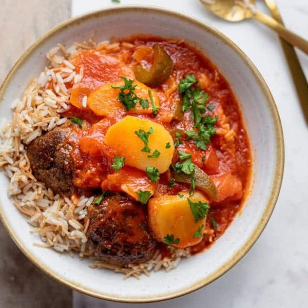 A bowl of kafta and potato stew served over vermicelli rice with fresh parsley garnish.